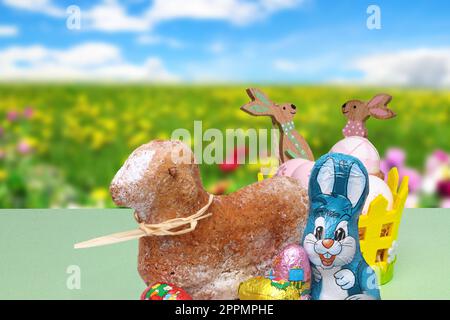 Easter card. A traditional Easter lamb cake, a easter bunny, chocolate sweets and basket with eggs and wooden bunnies over abstract blurred spring background. Stock Photo