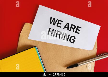 "Hiring Announcement on Red Background" - A white paper with a hiring announcement enclosed in an envelope, accompanied by office stationery, set agai Stock Photo