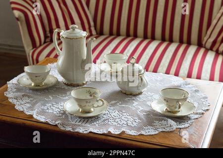 10.08.2021 Miclosoara Romania. Porcelain coffee set. Hackefors gold rim hand painted china cups, jug, sugar bowl on a crochet tablecloth. Stock Photo