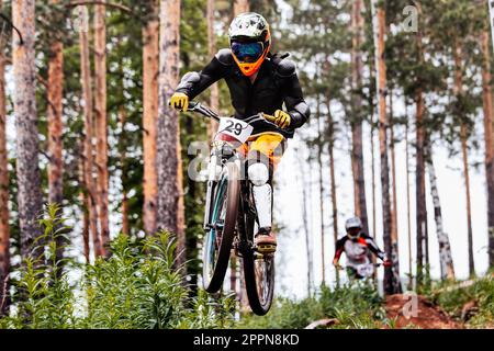 male racer athlete riding downhill race, jump over hill, on him protection jacket, and knee, shin guard Stock Photo