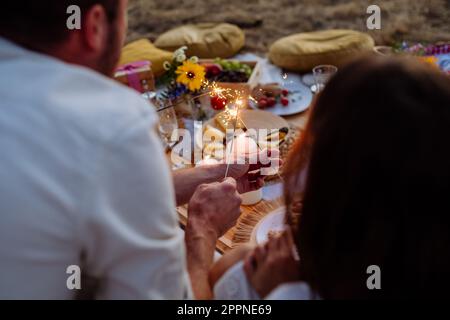Rear view of family with sparklers having picnic in the nature. Stock Photo