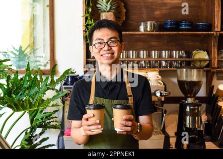 Vietnamese smiling waiter holding paper cups with coffee in a cafe Stock Photo