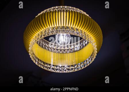 Interior design: round yellow ceiling lamp made of plastic with crystal cut elements  in the style of the 1950s in front of a dark background Stock Photo
