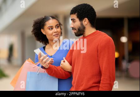 Middle Eastern Couple Using Smartphone Shopping Online Standing At Supermarket Stock Photo