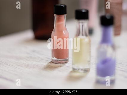 Three small bottles of colourful cream in a row with copy space. Wellness product on table. Bathroom concept. Cosmetic product. Healthy lifestyles. Stock Photo