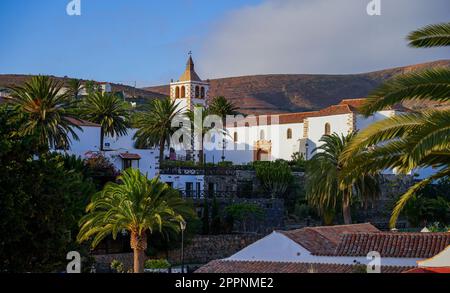 Panoramic wide view of the church of Saint Mary of Betancuria surrounded by palm trees at sunset in the former capital city of Fuerteventura island in Stock Photo