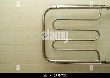 heated towel rail in the bathroom on the background of beige ceramic tiles. Stock Photo