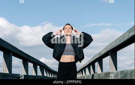 fit, sporty, mid adult woman standing wearing wireless headphones and listening to music. Stock Photo