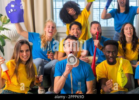 Soccer fan supporter friends cheering and watching football cup match at home Intenational - Group young people with multicolor t-shirts having fun wi Stock Photo