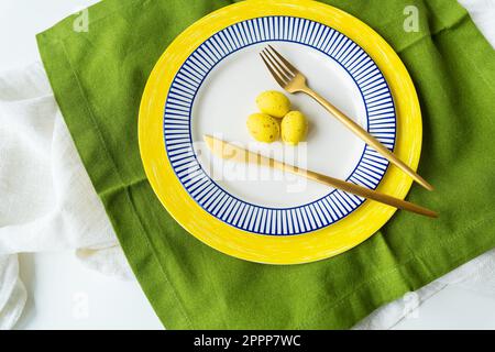 Easter serving concept. Festive table setting with bright napkins and yellow-blue plates with dishes and decorated eggs Stock Photo