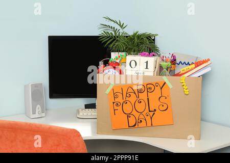 Box with different items and words Happy Fool's Day at workplace in office Stock Photo