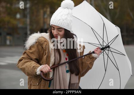 Woman with white umbrella caught in gust of wind on street Stock Photo