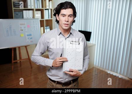 Young confident male business coach in smart casualwear showing financial document with graphs and explaining data to audience Stock Photo