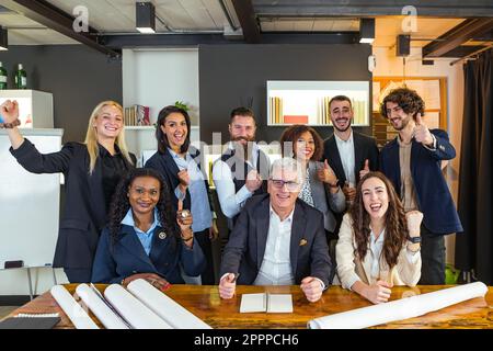 Multi-ethnic and mixed age group of entrepreneurs rejoicing at a success of their company. Sitting at the meeting table they smile in victory with the Stock Photo