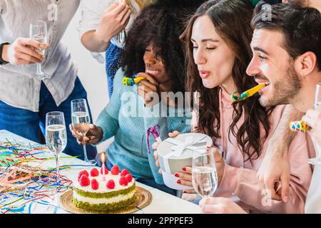 Birthday party with friends. Girl blowing out candles on cake and holding her present before unwrapping it Stock Photo
