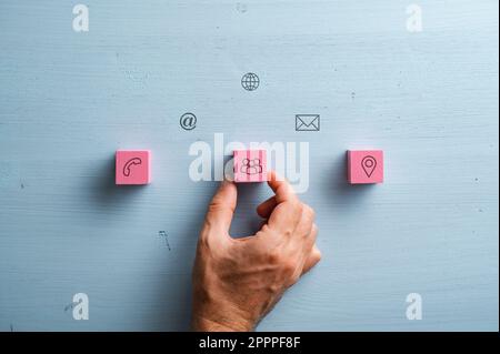 Contact and communication icons and symbols printed on pink wooden blocks and light blue wooden background. Stock Photo