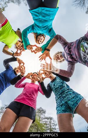 Group of female athletes runners in circle forming hearts with hands. Message of peace and love for sport. Women of different ages having fun after tr Stock Photo