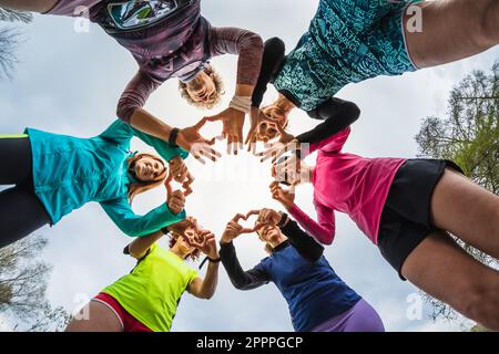 Group of female athletes runners in circle forming hearts with hands. Message of peace and love for sport. Women of different ages having fun after tr Stock Photo