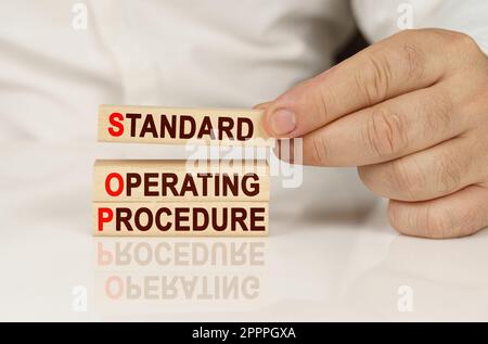 Business concept. In the hands of a person and on a reflective surface are wooden blocks with the inscription - Standard Operating Procedure Stock Photo