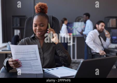 African American trader looking at document and discussing financial market with customer by the phone Stock Photo