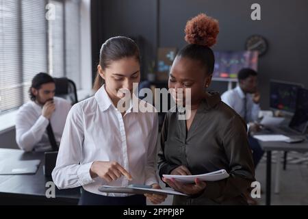 Two young colleagues analyzing stock market together examining documents while standing in office Stock Photo