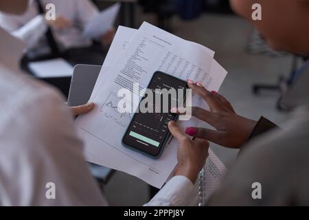 Close-up of colleagues examining financial graphs on the screen of smartphone and discussing stock market Stock Photo