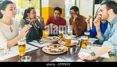 Diverse team smart worker having pizza together in an office cafeteria sitting on a table. Cheerful workers staff sharing meal. Enjoying and having fu Stock Photo