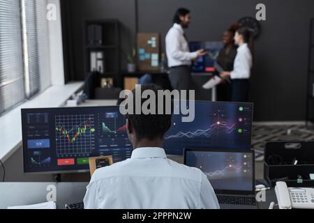 Rear view of African American young trader working on computer with graphs and charts at his workplace in office Stock Photo
