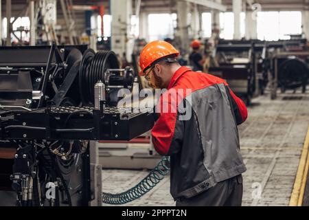 Industrial worker assembles agricultural machine in workshop. Stock Photo