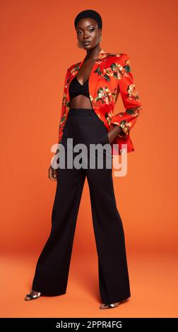 A female model wearing a black cropped tank top and matching pants, standing in a brightly lit orange background Stock Photo