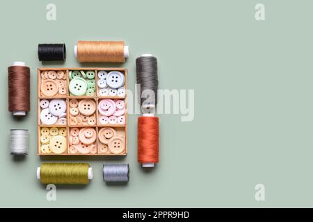 Composition with box of different buttons and thread spools on grey background Stock Photo