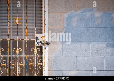 Padlock on rusted metal screen door with stained cinder block wall Stock Photo
