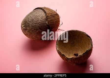 broken coconut on a pink background. Coconut cleaning. Stock Photo