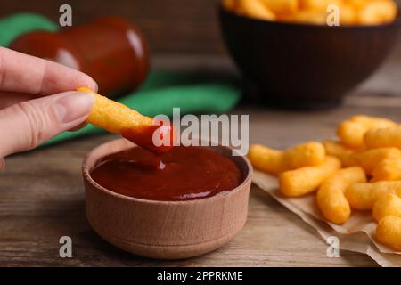 Woman dipping tasty cheesy corn stick in red sauce at wooden table, closeup Stock Photo