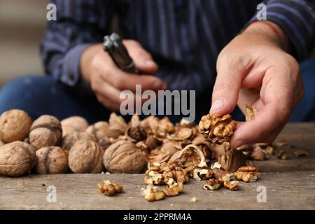 Man cracking walnuts at wooden table, closeup Stock Photo