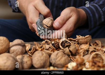 Man cracking walnuts at table, closeup view Stock Photo