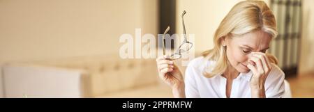 Tired mature businesswoman took off her glasses, massaging nose bridge, suffering from dry eyes syndrome Stock Photo
