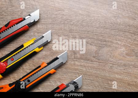 Many different utility knives on wooden table, flat lay. Space for text Stock Photo