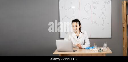 Chemistry teacher school university online. Female scientist teacher speaks with students has web chat using laptop computer sitting at desk in Stock Photo
