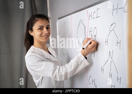 Chemistry teacher writing formulas with marker on the whiteboard while having lecture. Concept of explore science. Stock Photo