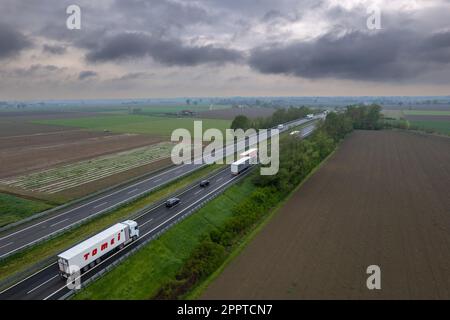 Piacenza, Italy - April 2023 Cargo trucks and cars in the motorway a1 autostrada del sole aerial point of view in between padain plain rural fields Stock Photo