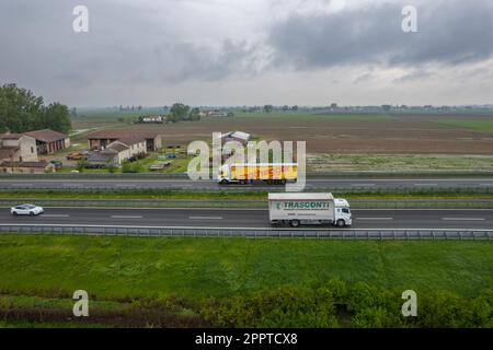 Piacenza, Italy - April 2023 Cargo trucks and cars in the motorway a1 autostrada del sole aerial point of view in between padain plain rural fields Stock Photo