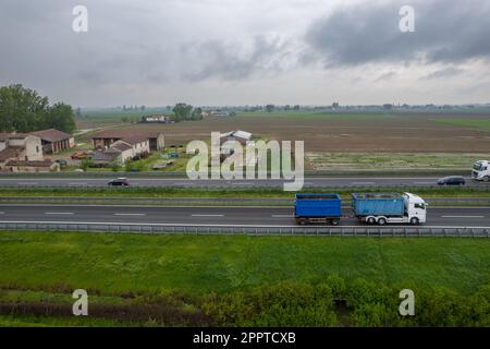 Piacenza, Italy - April 2023 Cargo trucks and cars in the motorway a1 autostrada del sole aerial point of view in between padain plain rural fields Stock Photo