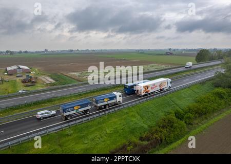 Piacenza, Italy - April 2023 Cargo trucks and cars in the motorway a1 autostrada del sole aerial point of view in between padain plain rural fields Stock Photo