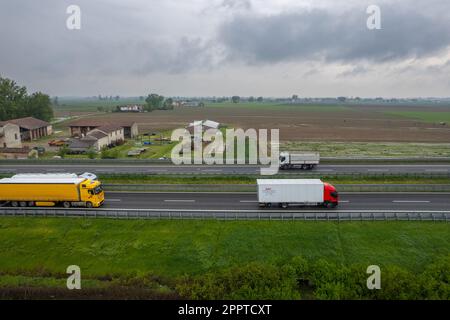 Piacenza, Italy - April 2023 Cargo trucks and cars in the motorway a1 autostrada del sole aerial point of view in between padain plain rural fields Stock Photo