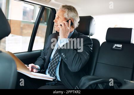 Travel fit for a stylish exec. a mature businessman using a mobile phone in the back seat of a car. Stock Photo