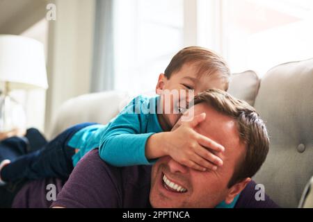 Peekaboo, guess who. an adorable little boy and his father playing together on the sofa at home. Stock Photo