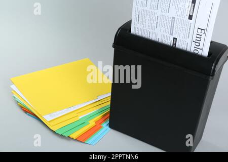 Shredder with sheet of paper and colorful folders on grey background Stock Photo