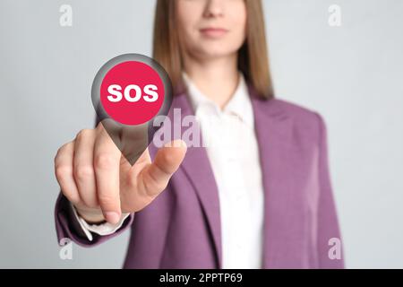 Young woman pressing virtual SOS button in case of danger on grey background, closeup Stock Photo