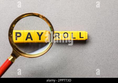 Word Payroll made with yellow cubes on light grey background, flat lay. View through magnifying glass Stock Photo